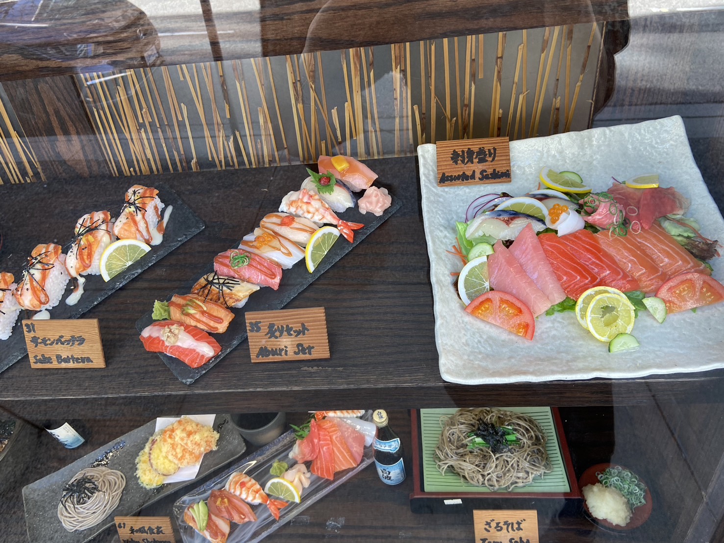 Close-up of a hyperrealistic sushi and sashimi food replica window display, showing the wet-look sheen a hero prop needs