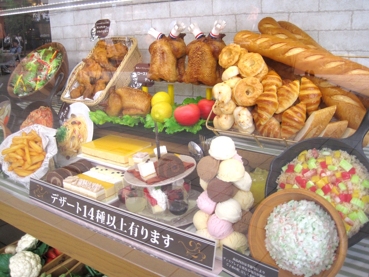 A bakery window filled with dessert and pastry food replicas under warm lighting