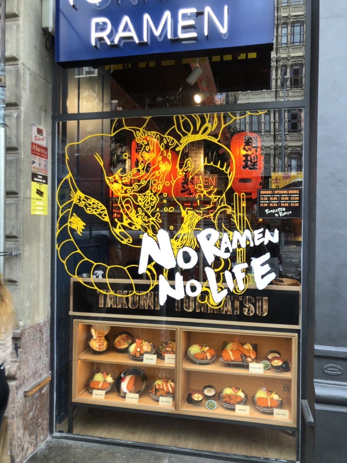 Hyperrealistic ramen food replica in a Barcelona restaurant window display, chopsticks lifting noodles above the bowl