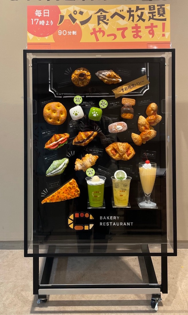 A freestanding display case of bread, pastry and drink food replicas at a bakery entrance